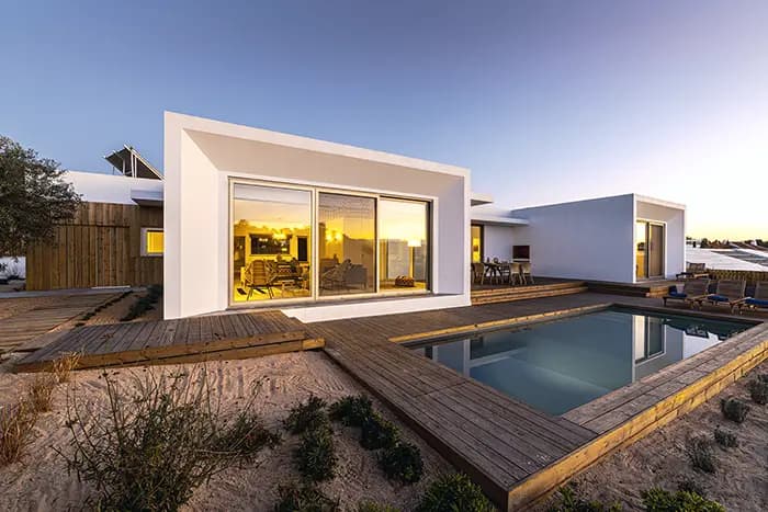 Modern white villa with large windows, a wooden deck and a swimming pool at dusk in Alentejo province, Portugal.