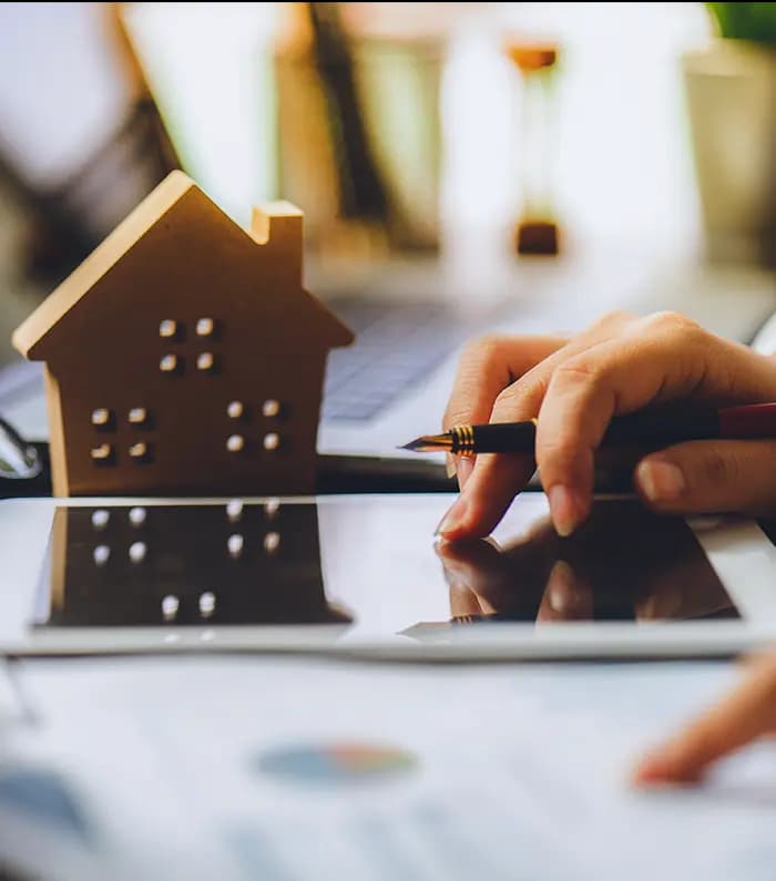A miniature 3d house mockup on the side of a tablet being used by female hands